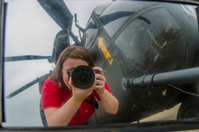Amanda with a camera reflected in the rearview mirror of a Blackhawk Helicopter.